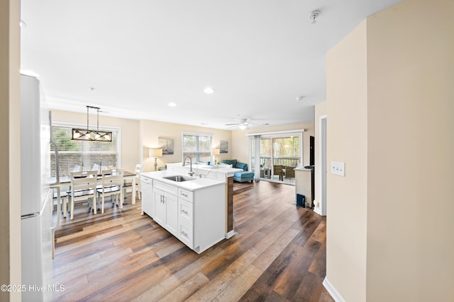 kitchen with sink, decorative light fixtures, a kitchen island with sink, white cabinets, and ceiling fan with notable chandelier