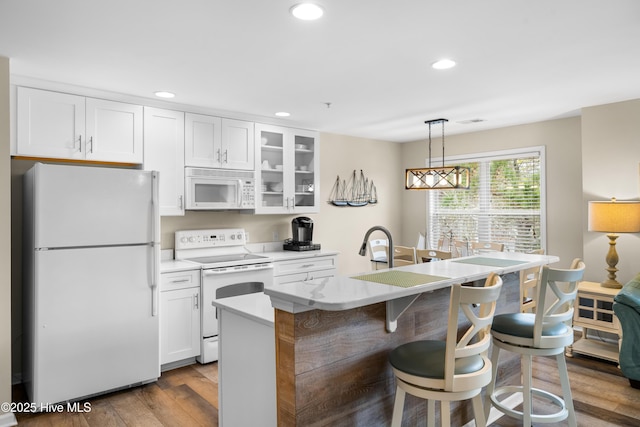 kitchen with white appliances, wood-type flooring, a center island with sink, white cabinets, and hanging light fixtures