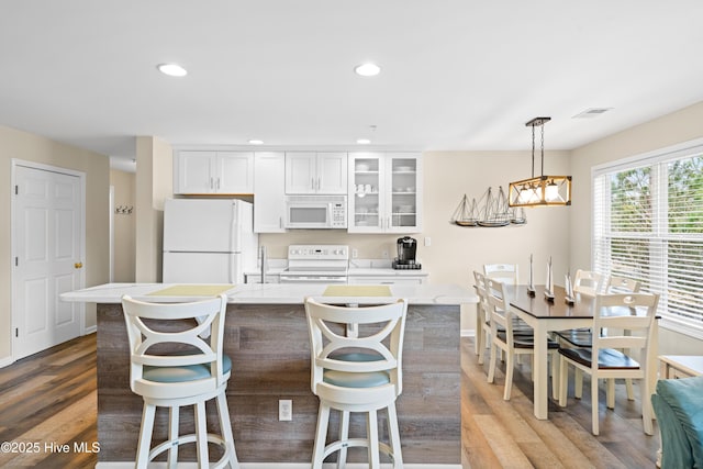 kitchen with wood-type flooring, decorative light fixtures, white appliances, a kitchen bar, and white cabinets