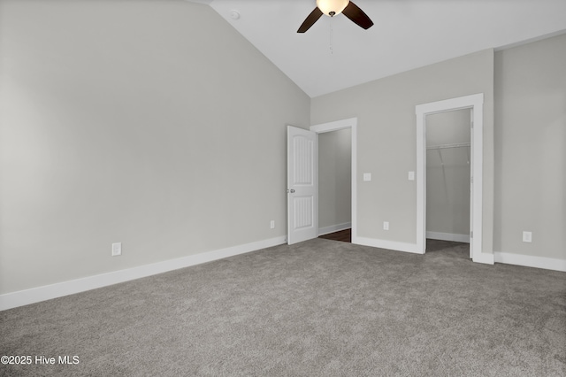 unfurnished bedroom featuring lofted ceiling, ceiling fan, a closet, dark colored carpet, and a walk in closet