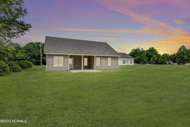 back house at dusk featuring a lawn and a patio