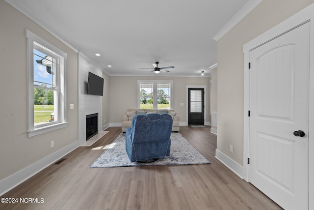 living room with ceiling fan, a large fireplace, light hardwood / wood-style floors, and ornamental molding