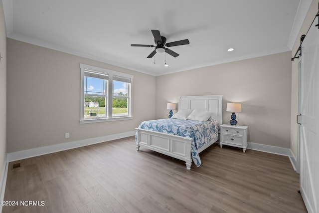 bedroom with a barn door, ceiling fan, crown molding, and hardwood / wood-style flooring