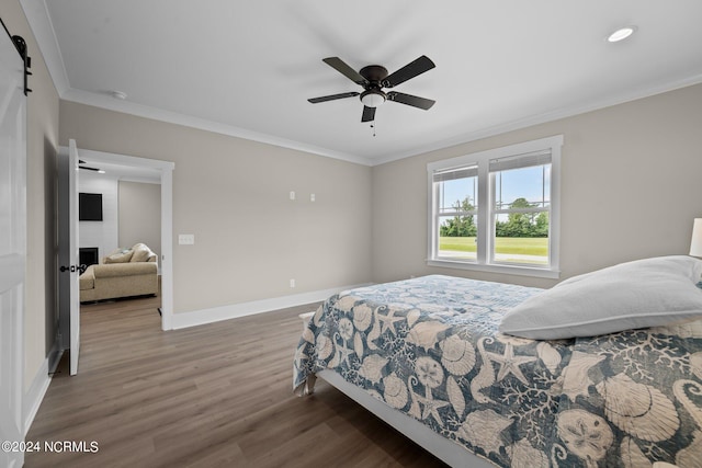 bedroom featuring ceiling fan, a barn door, dark hardwood / wood-style flooring, and ornamental molding