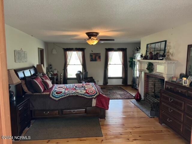 bedroom featuring a brick fireplace, ceiling fan, a textured ceiling, and light wood-type flooring