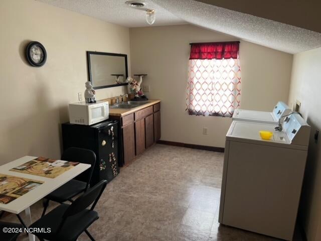 office featuring light tile flooring, washer and clothes dryer, sink, a textured ceiling, and lofted ceiling