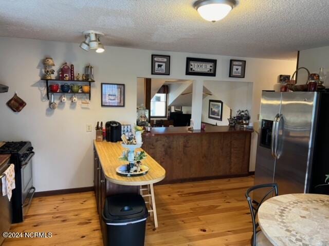 kitchen with gas stove, stainless steel fridge with ice dispenser, a textured ceiling, and light wood-type flooring