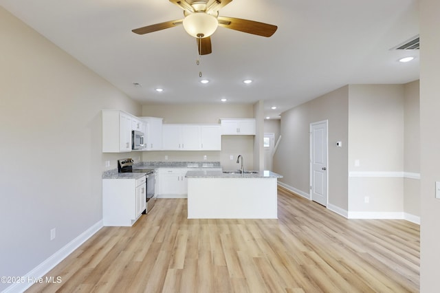 kitchen with light stone countertops, stainless steel appliances, sink, a center island with sink, and white cabinetry