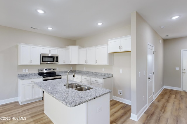 kitchen with light stone countertops, sink, a kitchen island with sink, white cabinets, and appliances with stainless steel finishes