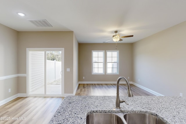 kitchen with light stone countertops, light hardwood / wood-style flooring, ceiling fan, and sink