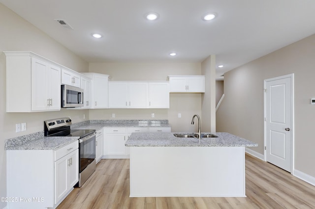 kitchen with appliances with stainless steel finishes, light stone counters, sink, a center island with sink, and white cabinets