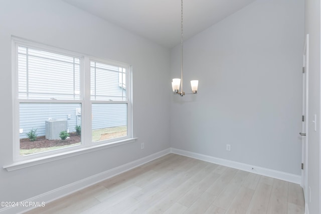 empty room featuring plenty of natural light, an inviting chandelier, and light hardwood / wood-style floors