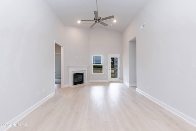 unfurnished living room featuring ceiling fan, a high ceiling, a high end fireplace, and light hardwood / wood-style flooring