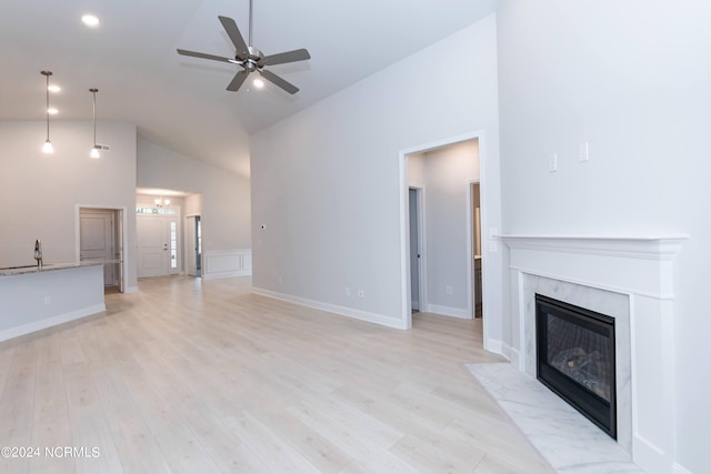 unfurnished living room featuring ceiling fan, light wood-type flooring, a premium fireplace, high vaulted ceiling, and sink