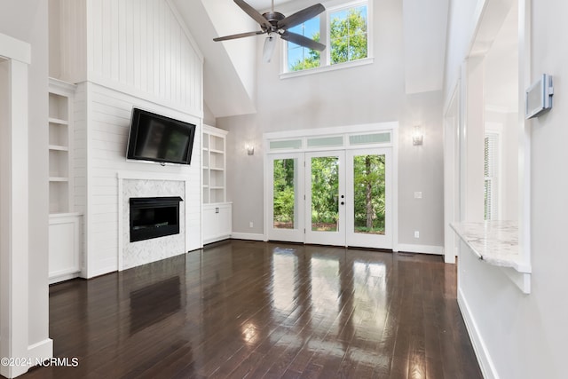 unfurnished living room with built in shelves, ceiling fan, dark hardwood / wood-style floors, a high ceiling, and a fireplace