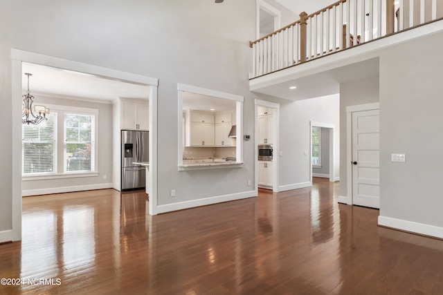 unfurnished living room featuring an inviting chandelier, dark hardwood / wood-style floors, and a high ceiling