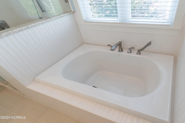 bathroom featuring a relaxing tiled tub and a healthy amount of sunlight