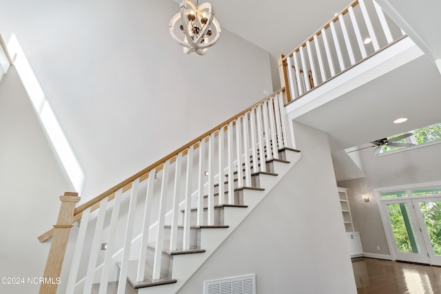 stairs with a high ceiling, hardwood / wood-style floors, and ceiling fan with notable chandelier