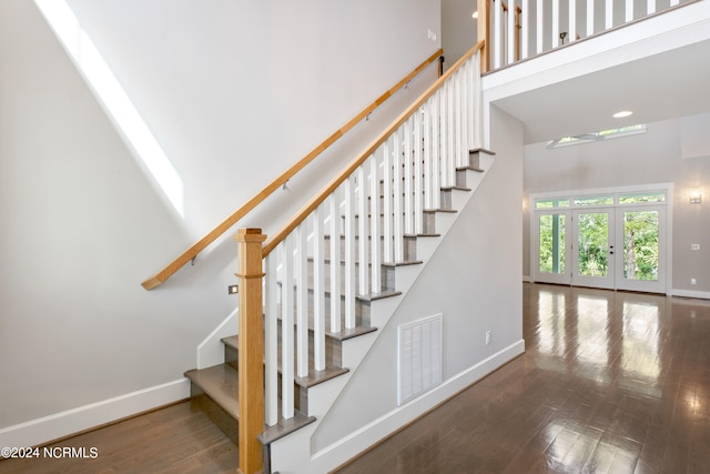 staircase featuring wood-type flooring, french doors, and a high ceiling