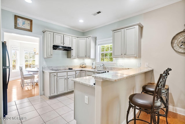 kitchen with kitchen peninsula, light stone countertops, a kitchen bar, black appliances, and light tile floors