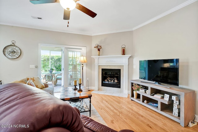 living room with light hardwood / wood-style flooring, ceiling fan, a tile fireplace, and crown molding