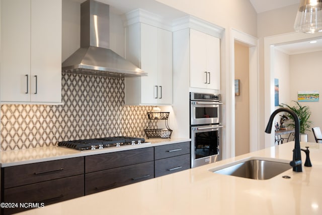 kitchen with backsplash, wall chimney range hood, sink, white cabinetry, and appliances with stainless steel finishes