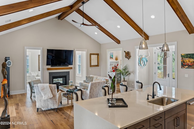 kitchen with vaulted ceiling with beams, an island with sink, sink, hanging light fixtures, and ceiling fan