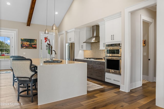 kitchen with white cabinets, appliances with stainless steel finishes, wall chimney exhaust hood, and an island with sink