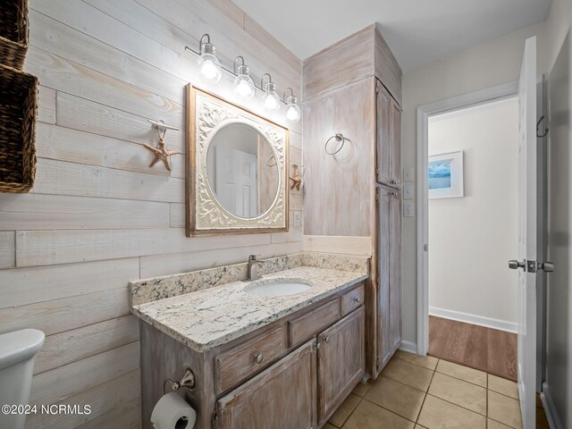 bathroom with tile patterned flooring, wood walls, vanity, and toilet