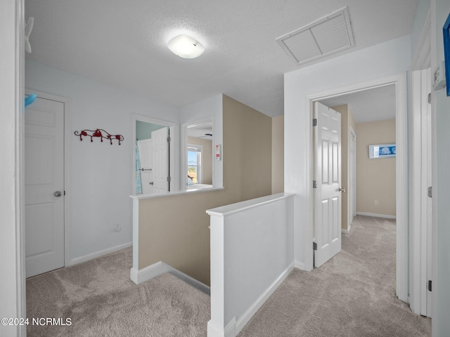 hallway with a textured ceiling and light carpet