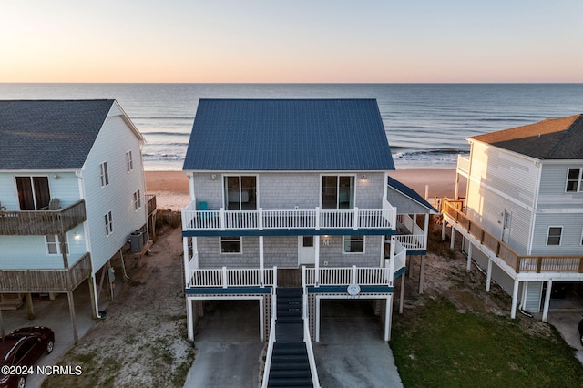 back house at dusk with a balcony, a carport, cooling unit, and a water view