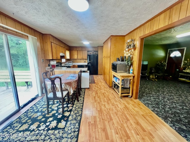 kitchen with wood walls, stove, light carpet, black refrigerator with ice dispenser, and a textured ceiling