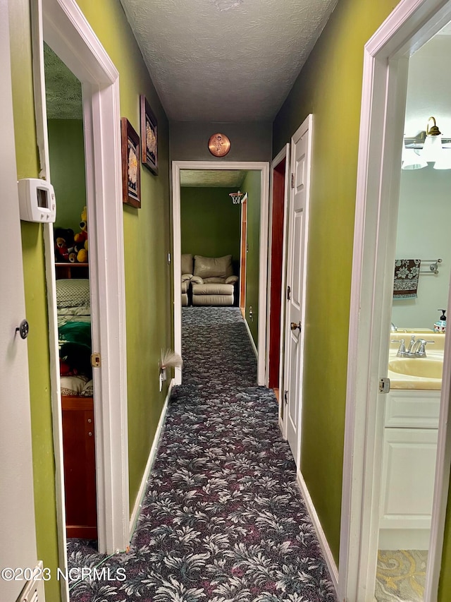 hallway with a textured ceiling, dark colored carpet, and sink