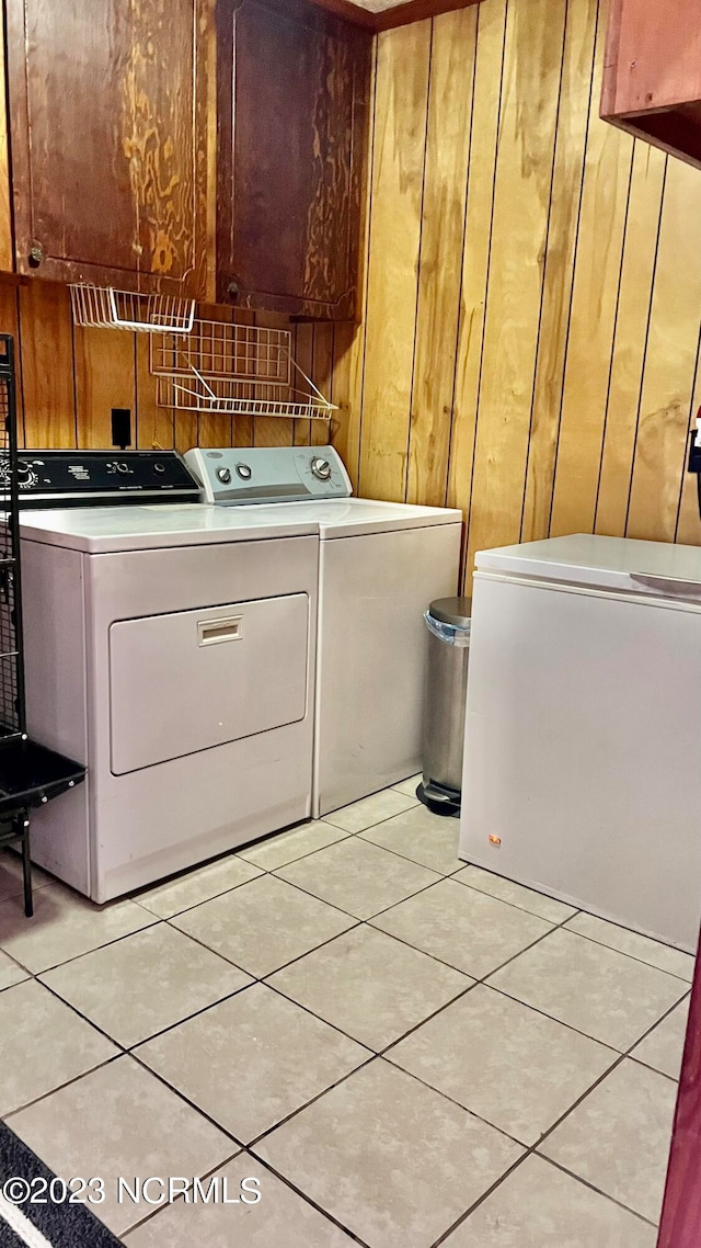 laundry room featuring wood walls, washing machine and dryer, cabinets, and light tile floors