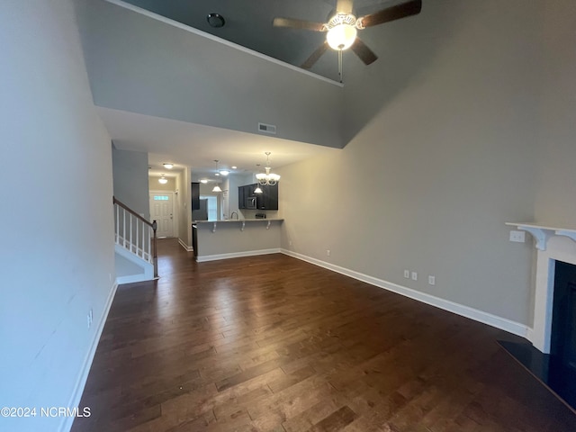 unfurnished living room featuring ceiling fan with notable chandelier, dark wood-type flooring, and a high ceiling