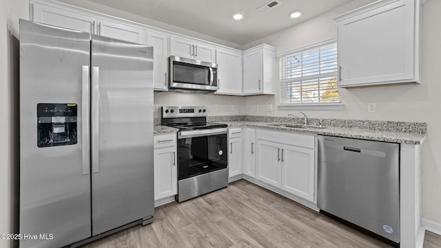 kitchen with visible vents, a sink, stainless steel appliances, light wood-style floors, and white cabinetry