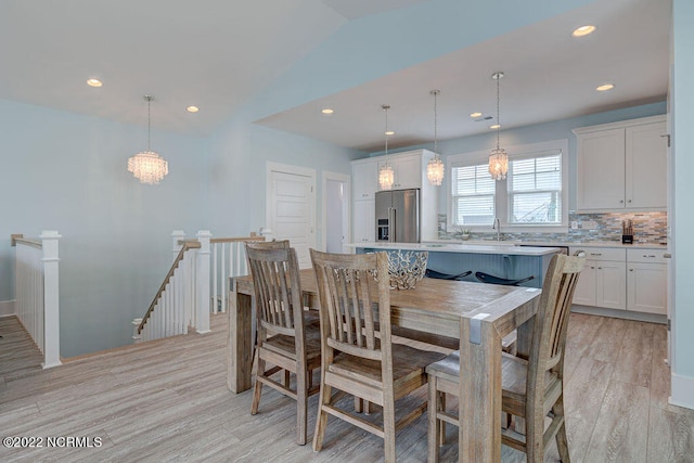 dining space with lofted ceiling, light hardwood / wood-style flooring, and an inviting chandelier