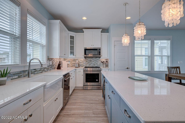 kitchen with hanging light fixtures, white cabinets, light wood-type flooring, stainless steel appliances, and tasteful backsplash