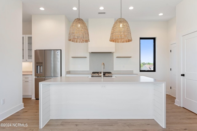 kitchen featuring stainless steel refrigerator with ice dispenser, light hardwood / wood-style floors, and an island with sink