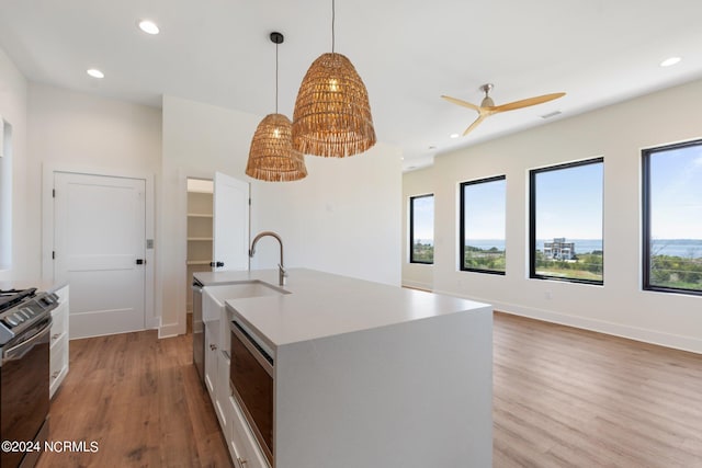 kitchen featuring ceiling fan, stainless steel appliances, light hardwood / wood-style floors, a kitchen island with sink, and pendant lighting