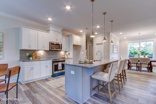 kitchen with an island with sink, light hardwood / wood-style floors, white cabinets, and backsplash