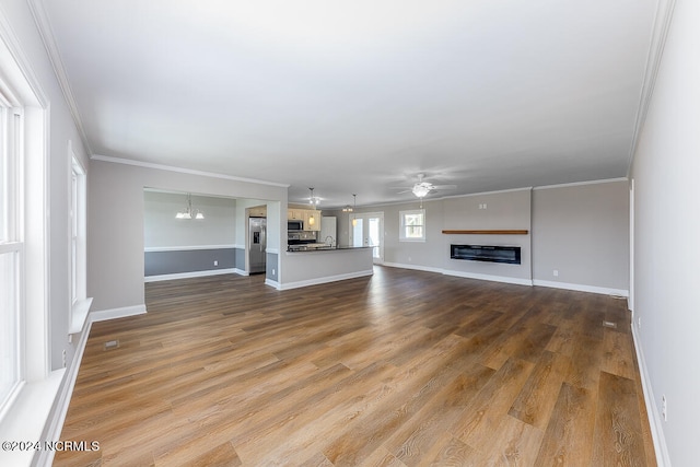 unfurnished living room with ceiling fan with notable chandelier, sink, hardwood / wood-style flooring, and ornamental molding