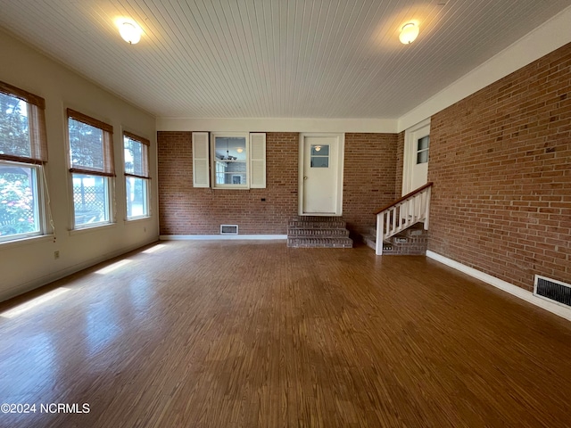 empty room with dark hardwood / wood-style flooring and brick wall