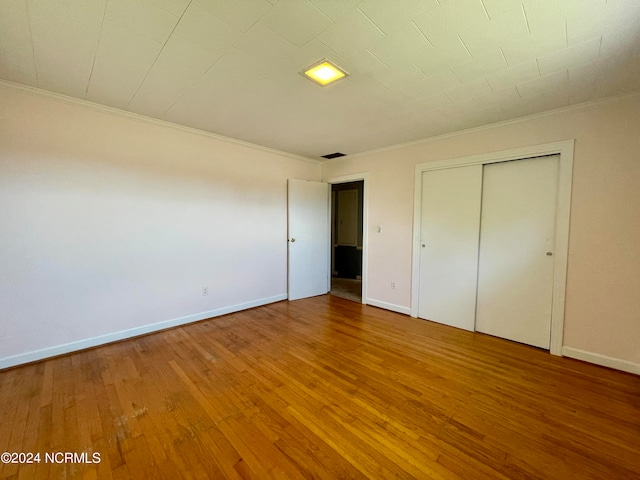 unfurnished bedroom with a closet, hardwood / wood-style floors, and crown molding