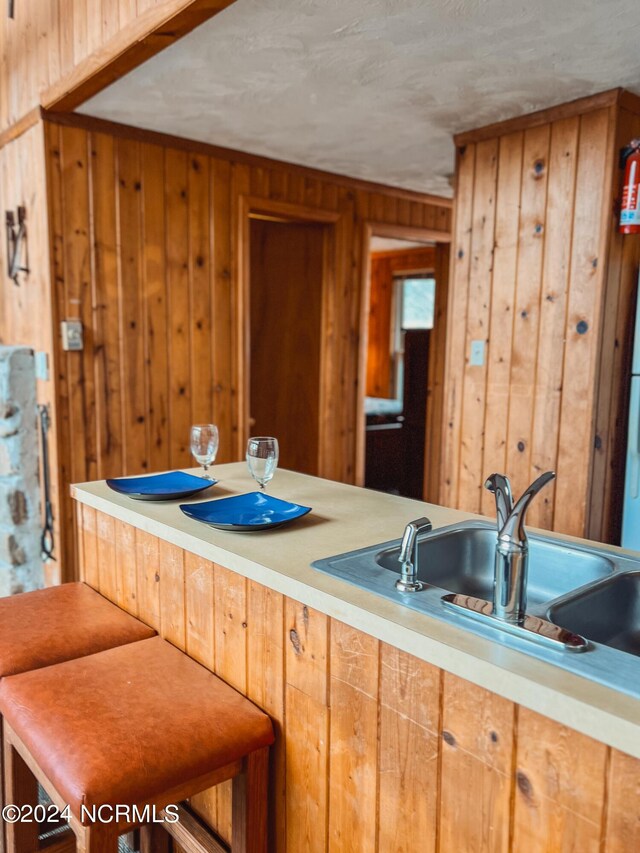 kitchen with a wood stove, wood walls, lofted ceiling with beams, sink, and dishwasher