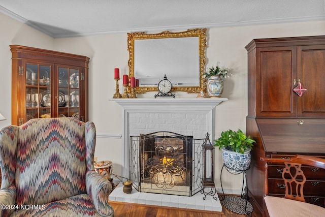 sitting room with ornamental molding, wood-type flooring, and a brick fireplace