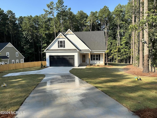 modern inspired farmhouse featuring concrete driveway, fence, a wooded view, a garage, and a front lawn