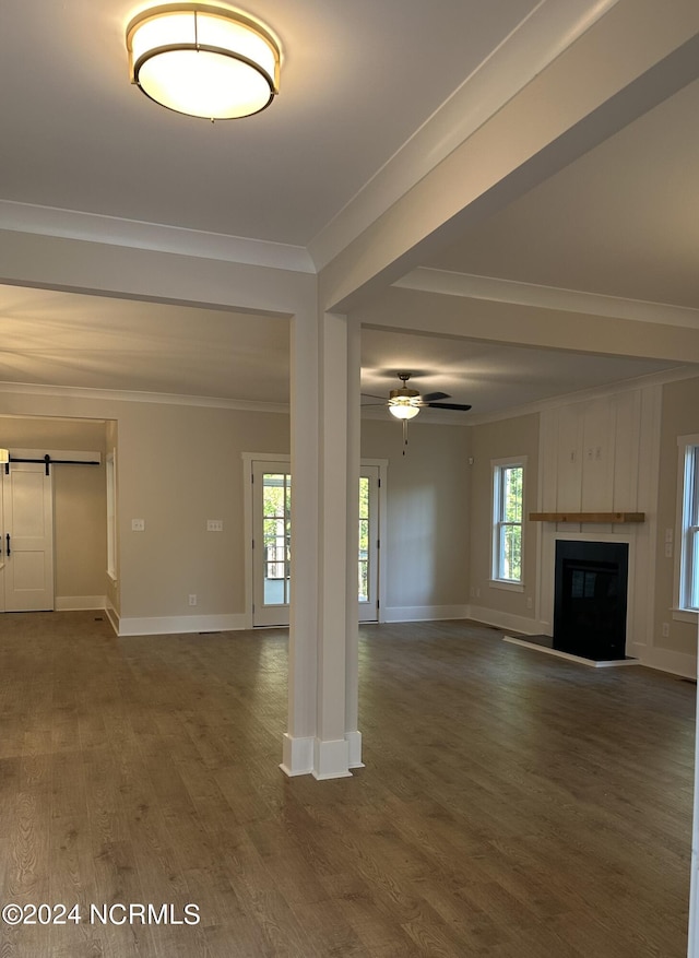 unfurnished living room with a barn door, a glass covered fireplace, ceiling fan, ornamental molding, and wood finished floors