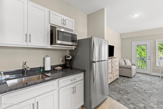 kitchen featuring appliances with stainless steel finishes, dark stone countertops, white cabinets, sink, and light tile floors