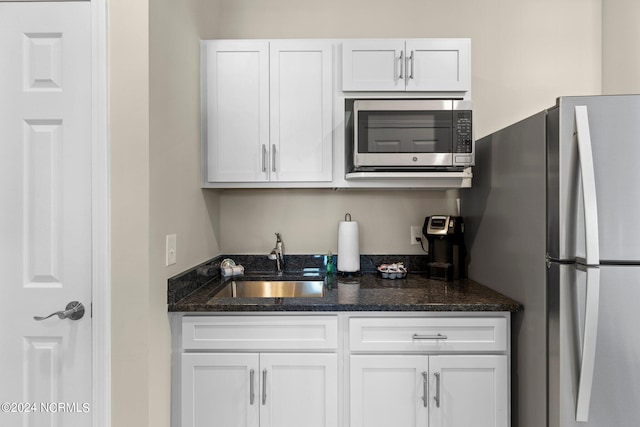 kitchen featuring dark stone counters, stainless steel appliances, white cabinets, and sink